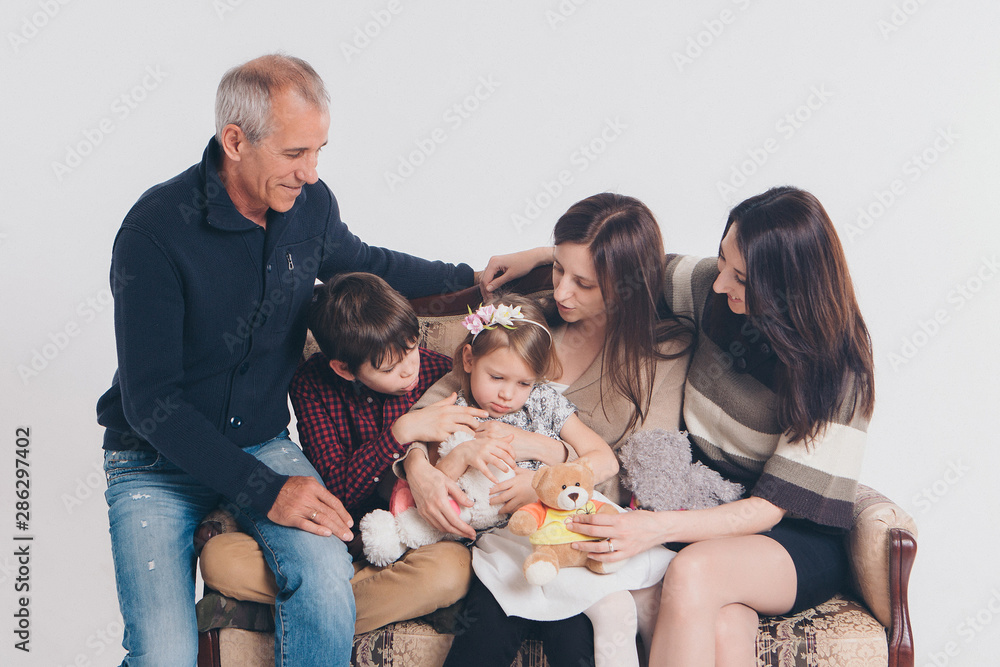 concept of happy childhood, family, love - group of people on a white background: adults and children with toys sitting on the same couch