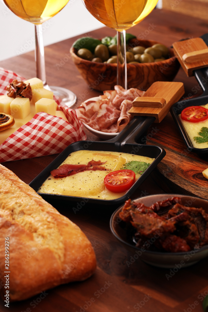 Delicious traditional Swiss melted raclette cheese on diced boiled or baked potato and baguette served in individual skillets with salami..