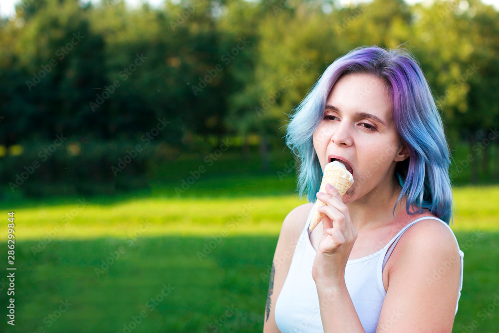 Beautiful happy young girl eating bite ice cream in a waffle roll with dyed multi-colored, colorful, blue, pink, purple hair. Sexy cheerful woman with bright freak hairstyle outdoor in a summer park. Beautiful happy young girl eating bite ice cream in a waffle roll with dyed multi-colored, colorful, blue, pink, purple hair. Sexy cheerful woman with bright freak hairstyle outdoor in a summer park.