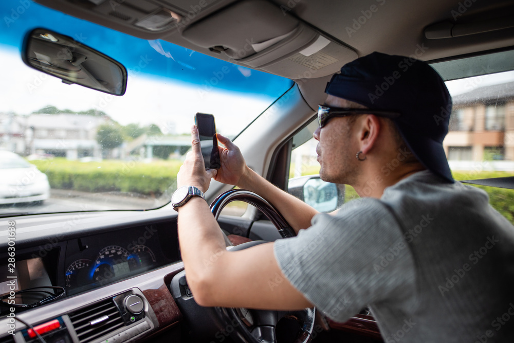 スマートフォンを見ながら自動車を運転する男性 スマートフォンを見ながら自動車を運転する男性