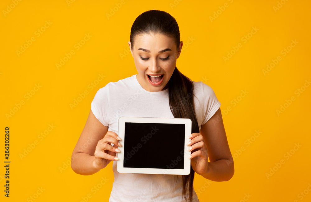 Surprised Girl Holding Tablet Looking At Empty Screen, Yellow Background