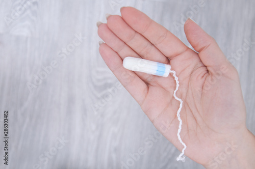 Tampon in a girl s hand closeup on a gray background.