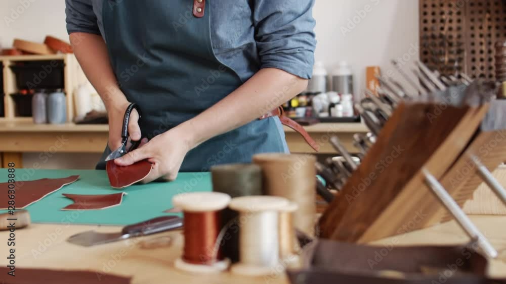 Tilt up of male shoemaker standing at worktop in workshop and snipping piece of leather he holding in hands Tilt up of male shoemaker standing at worktop in workshop and snipping piece of leather he holding in hands