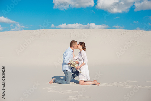 Handsome guy makes the girl a proposal for marriage, bending his knee, standing on the sand in the desert. Happy moments of family life © Viktoria