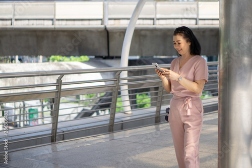 Healthy middle-aged women look happy wearing pink pants outdoor ambience with modern communication tools, smartphone