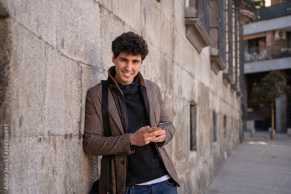 Young attractive happy hipster man talking on smart phone in european city