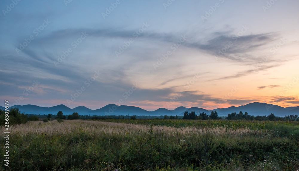 Obraz premium Clouds in the sky in the form of letters SS. Sunset landscape with silhouettes of mountains and fog. Fog in the valley
