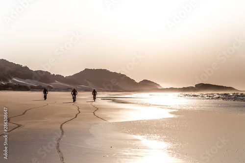 Three people cycling on the beach at sunrise