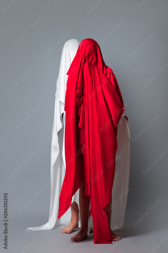 Female figures covered with a head of red and white cloth Red and white silhouette on a gray background. Minimalism. Concept Female figures covered with a head of red and white cloth Red and white silhouette on a gray background. Minimalism. Concept