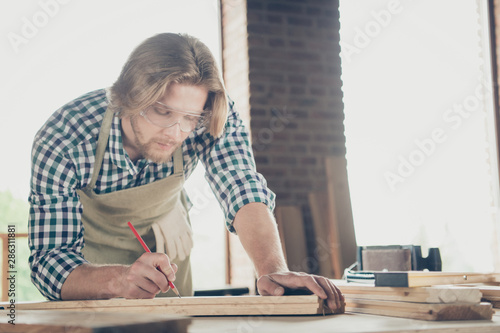 Portrait of his he nice handsome blond concentrated focused guy woodworker measuring board furniture shop studio at industrial brick loft style interior workplace indoors