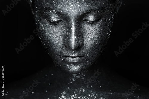 the girl's beautiful face is painted silver with sequins. shiny metal powder particles sparkle on the model's face