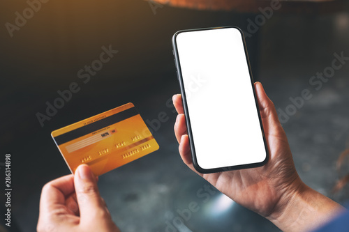 Mockup image of a hands holding credit card and a black mobile phone with blank desktop screen photo