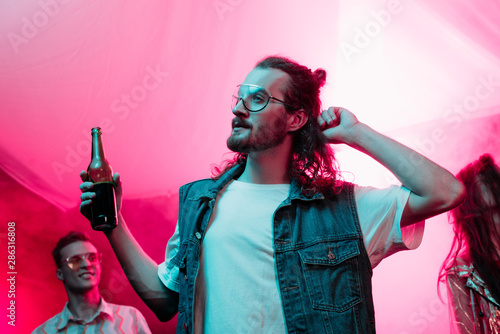 handsome man holding beer in nightclub and dancing during rave