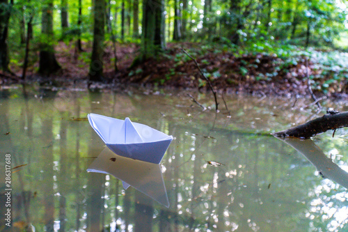 A paper boat sailing in the mountain forest lake. Small Paper Boat. Paper Ship Floating in the Sea. Origami Paper Boat Sailing. Mud water.