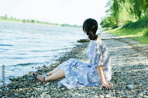 Fototapeta Naklejka Na Ścianę i Meble -  Young Asian woman sitting on the river bank, summer time