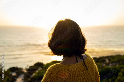 Tableau sur toile Girl with short hair and a yellow sweater watching the sunset on the beach below