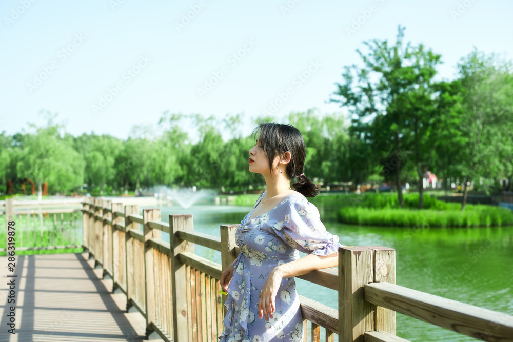 Young beautiful woman standing on the bridge, park background, near river