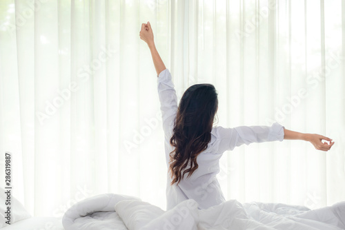 Asian women waking up stretching in bed room at home, early morning time and sunny day. Lifestyle Concept