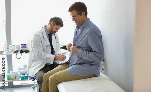Doctor reading medical report while patient undressing for checkup at hospital