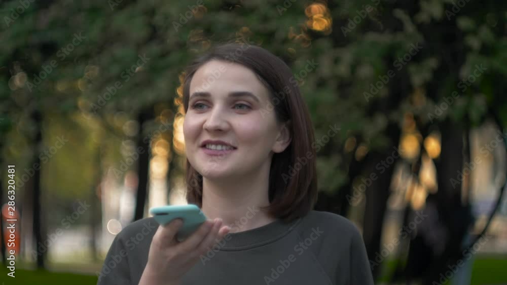Happy girl using a smart phone voice recognition audio message function on line walking on a street with urban city background, speech. Happy girl using a smart phone voice Happy girl using a smart phone voice recognition audio message function on line walking on a street with urban city background, speech. Happy girl using a smart phone voice