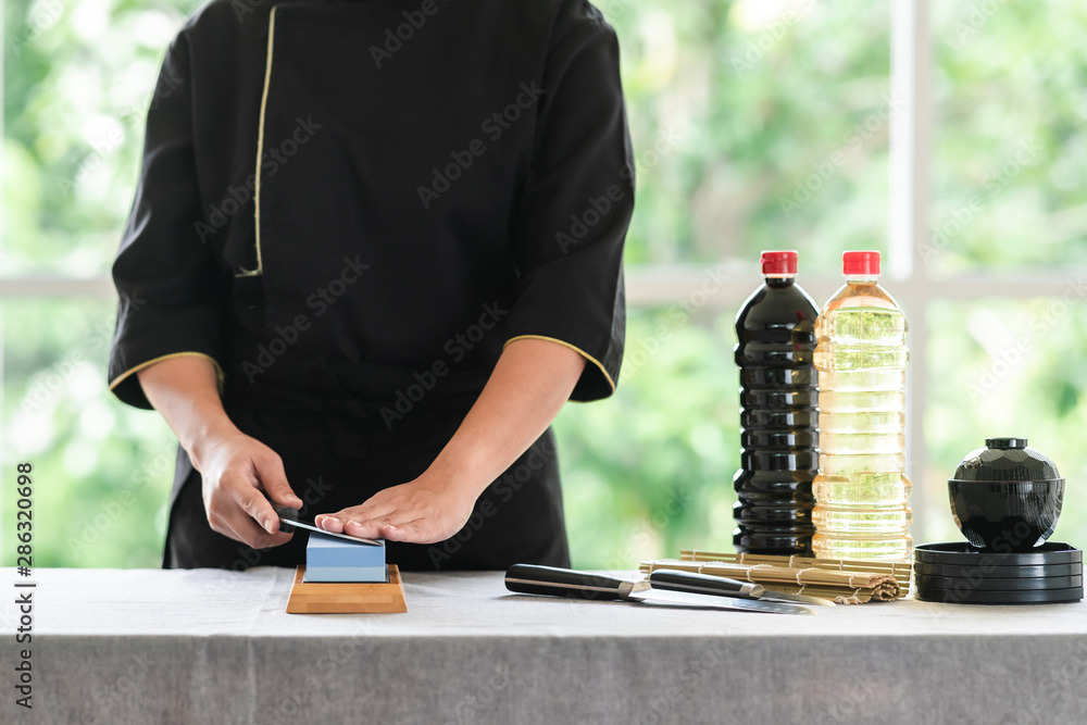 Chef sharpening knife on table. Japanese setting with asian woman. With green background. Chef sharpening knife on table. Japanese setting with asian woman. With green background.