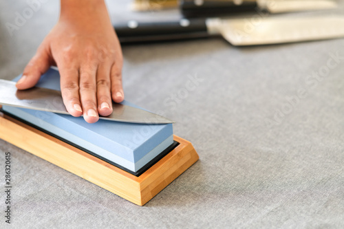 Chef sharpening knife on table. Japanese setting with asian woman. Close up of hand.