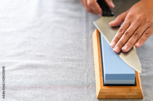 Chef sharpening knife on table. Japanese setting with asian woman. On grey table with copy space.