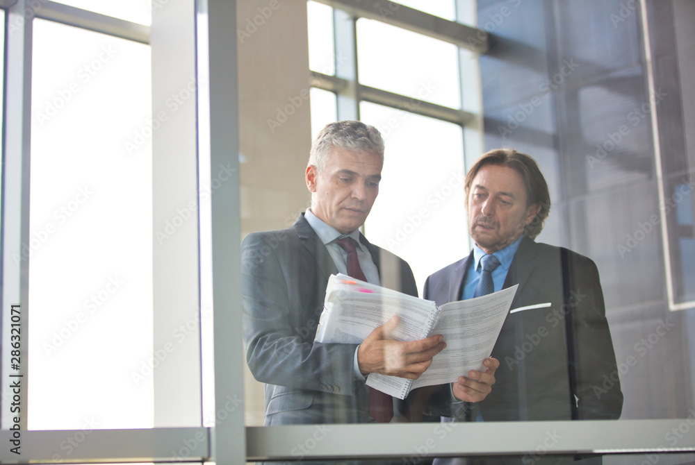 Fototapeta premium Mature businessmen discussing over document seen through glass in new office