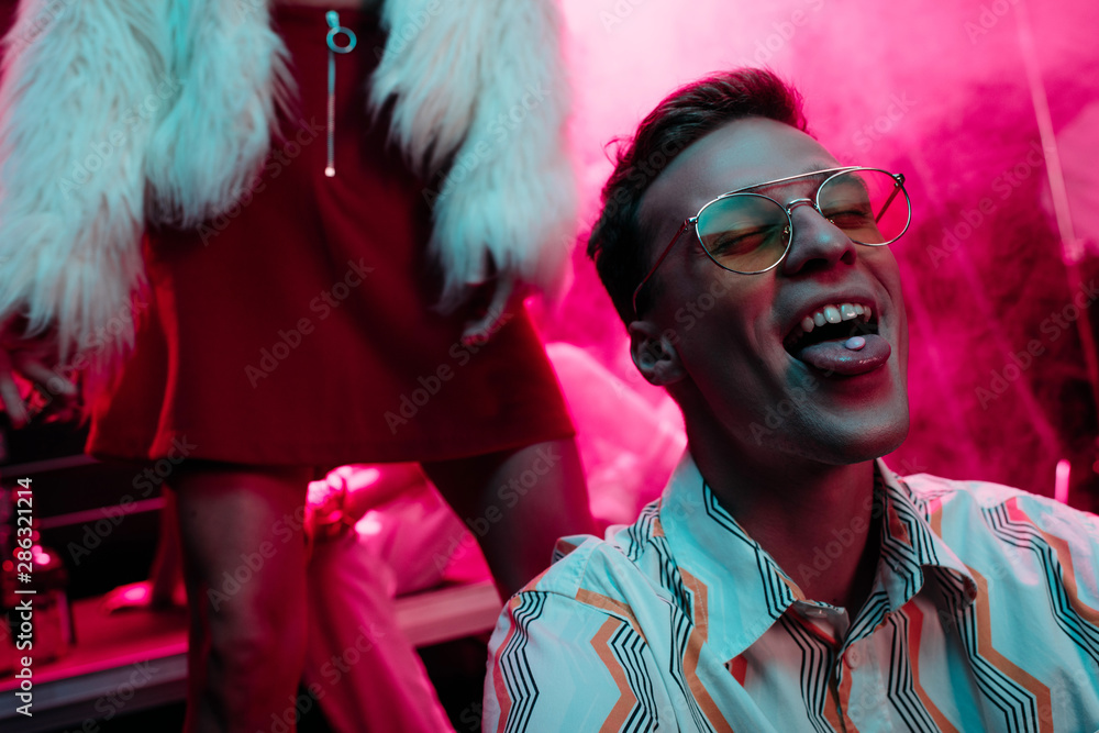 girl near man in sunglasses with lsd on tongue in nightclub with pink smoke