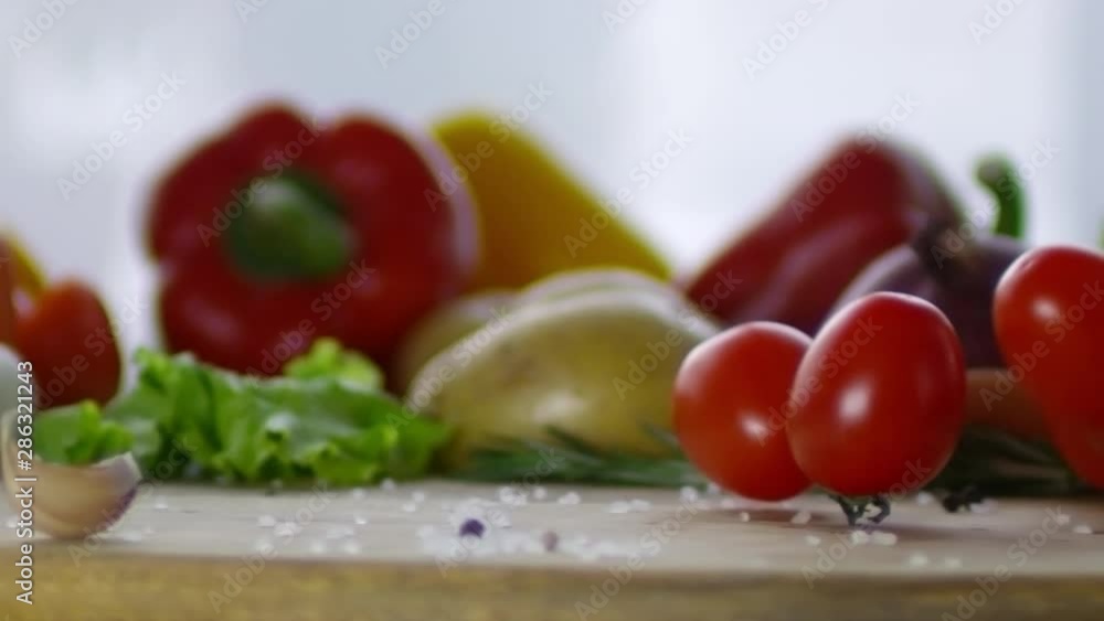 Close up tracking shot of plum tomatoes falling and rolling on wooden kitchen table with fresh vegetables on it Close up tracking shot of plum tomatoes falling and rolling on wooden kitchen table with fresh vegetables on it