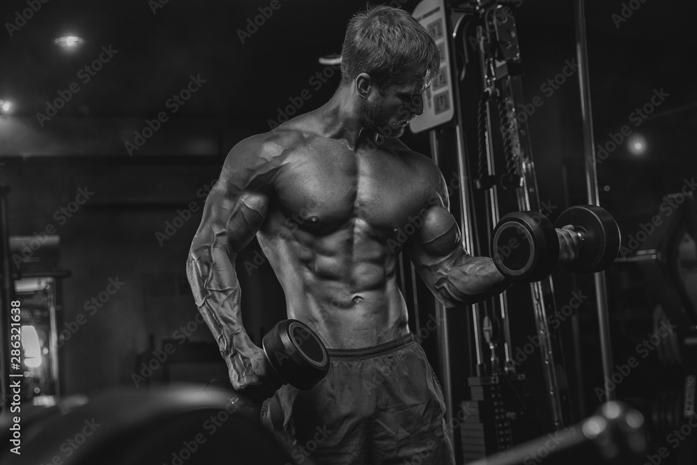 Fototapeta premium Brutal handsome Caucasian bodybuilder working out training in the gym gaining weight pumping up muscles and poses fitness and bodybuilding concept
