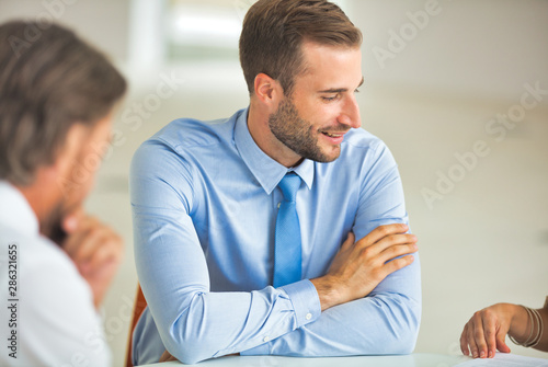 Young businessman smiling while colleagues discussing at table during meeting in office