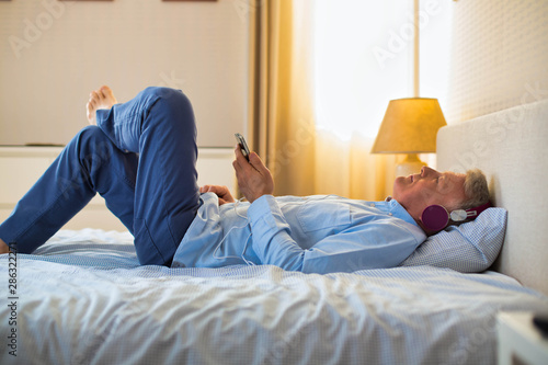 Mature man lying in bed while listening to music
