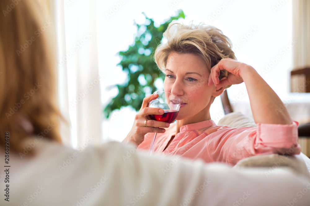 Mature women drinking wine while sitting in sofa at home