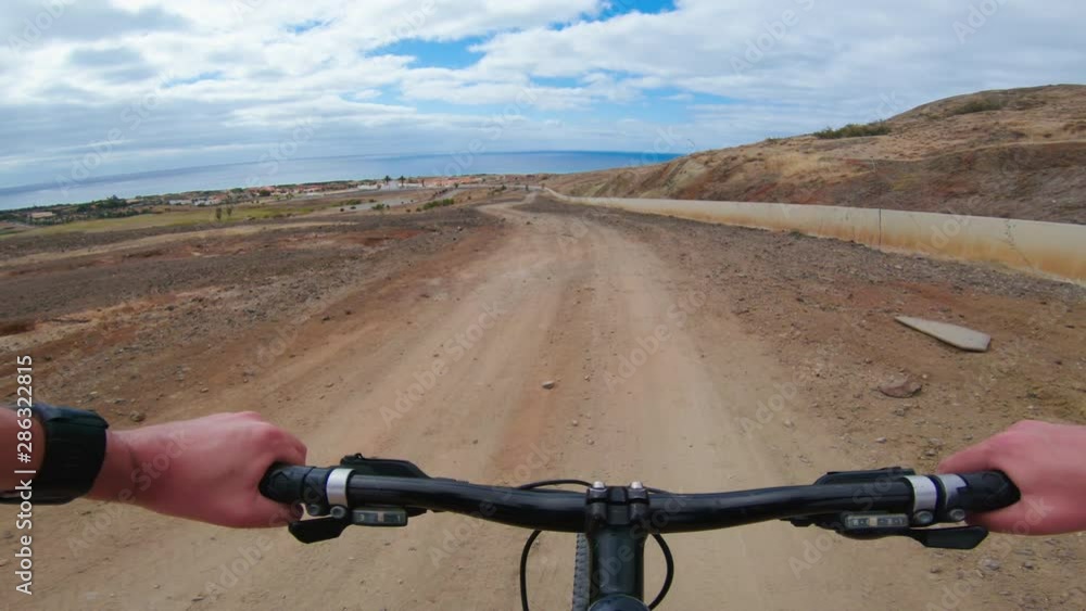 Racing on mountain bike down a gravel road seen from POV