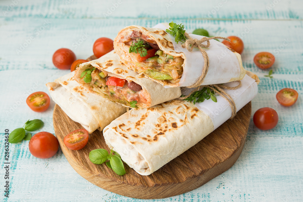 Traditional Mexican food burritos with beans and vegetables. Vegetarian rolls with red beans and vegetables lie on an aged wooden table.