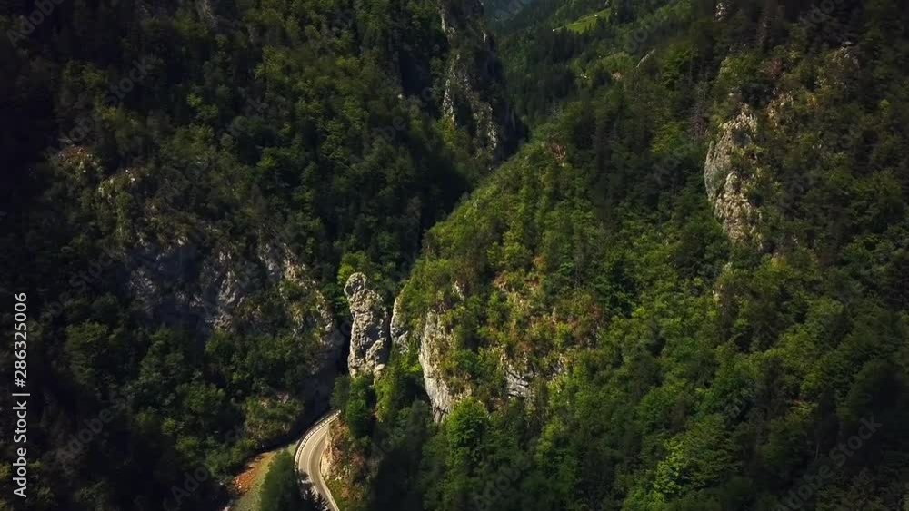 Forward drone shot, above a flowing river in Slovenia, surrounded by rocky mountains covered in green forests, near a country road, on a sunny day Forward drone shot, above a flowing river in Slovenia, surrounded by rocky mountains covered in green forests, near a country road, on a sunny day