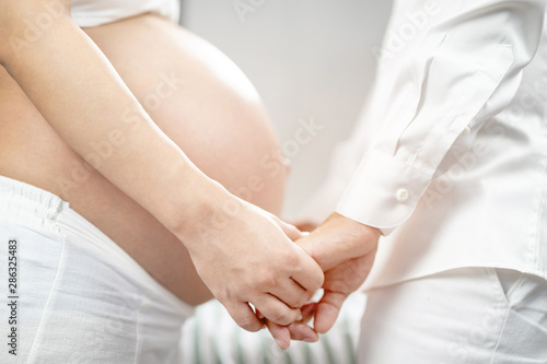 pregnant woman and her husband hand splice hugging the tummy Heart shaped show love for the unborn baby in the belly relaxing at home in bedroom. wait birth date expecting a baby stand in the outdoors