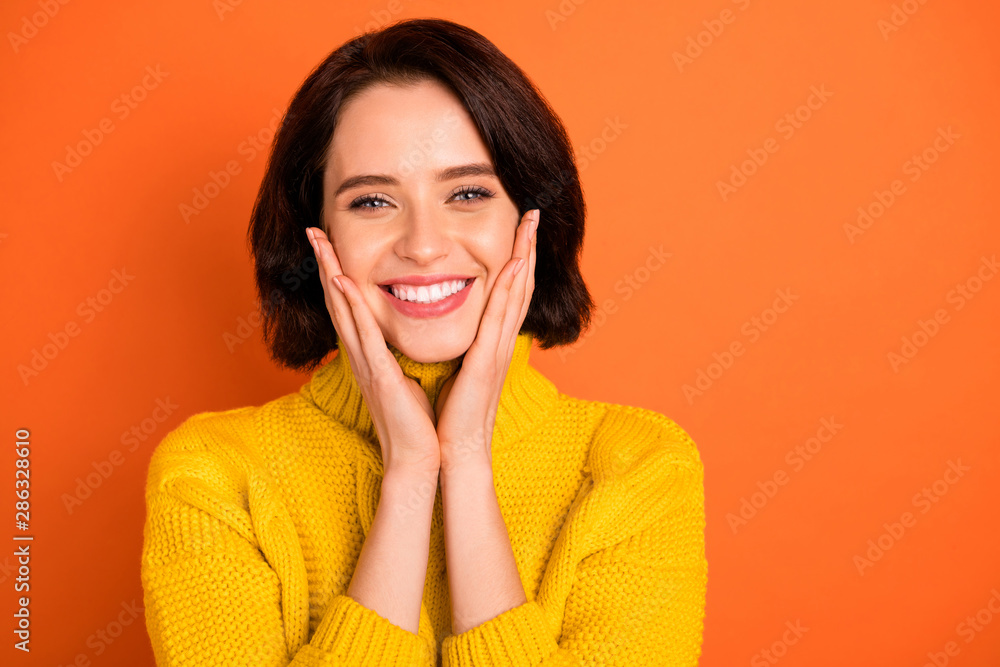 Photo of nice cute toothily smiling girl holding her cheeks showing her cuteness while isolated with orange background Photo of nice cute toothily smiling girl holding her cheeks showing her cuteness while isolated with orange background