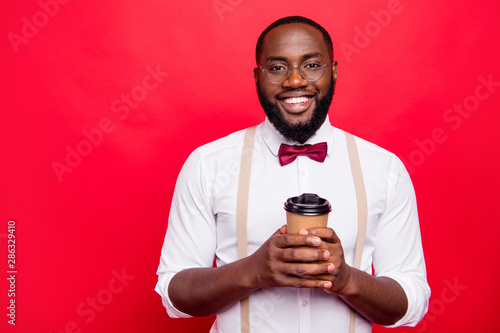Dark skin manager guy drinking hot beverage wear specs white shirt suspenders isolated red background © deagreez