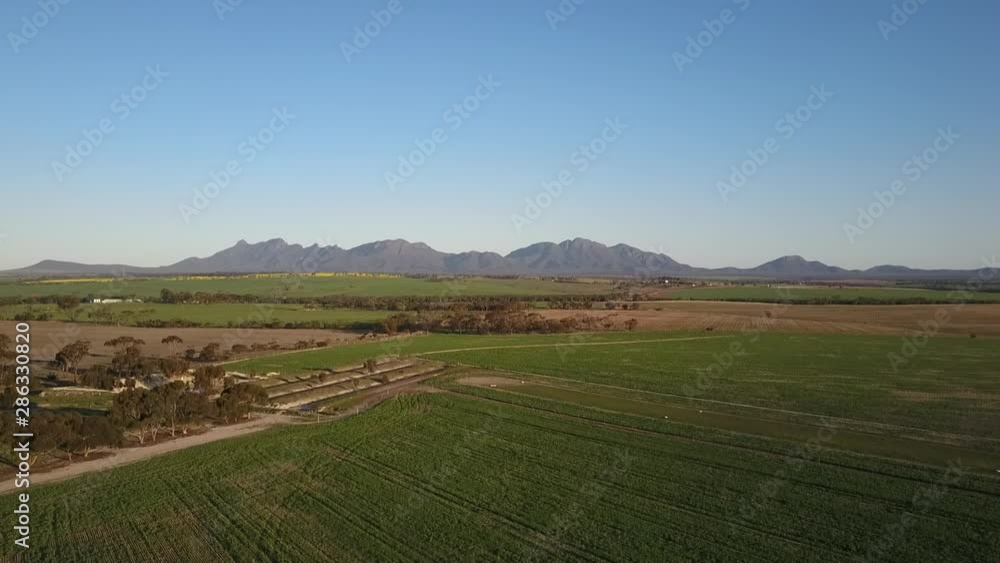 Aerial panoramic view of the scenic mountains of the Stirling Range National Park in Western Australia, flying above a wide open plain of agricultural fields on a sunny day with blue sky. Aerial panoramic view of the scenic mountains of the Stirling Range National Park in Western Australia, flying above a wide open plain of agricultural fields on a sunny day with blue sky.