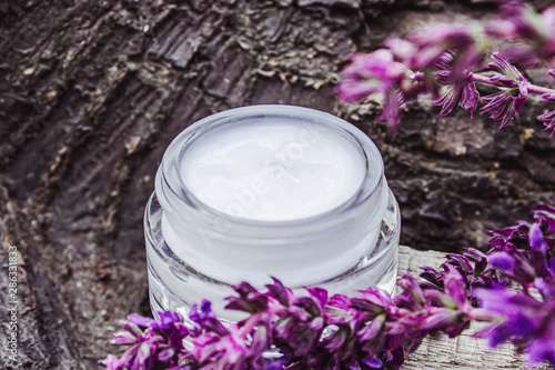 Cosmetic cream in a glass jar on a wooden background with lavender wildflowers. Face cream.