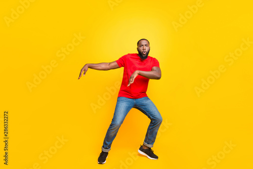 Full length body size photo of black man dancing with face serious while isolated with yellow background