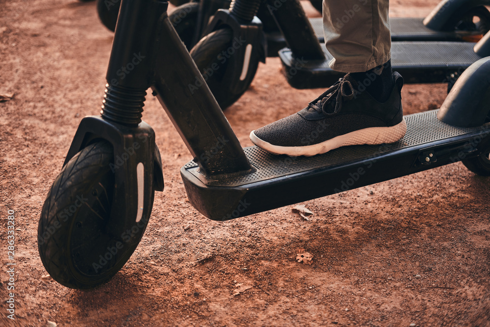 Obraz premium Closeup photo shoot of man's foot in sportive shoes on the scooter.
