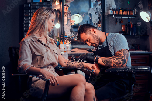Obraz na plátně Dilligent focused tattoo artist is creating new tattoo on young woman's hand at tatoo studio