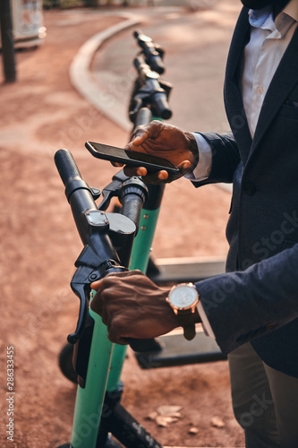 Closeup photo shoot of african man's hands with mobile phone. He is choosing the right scooter.