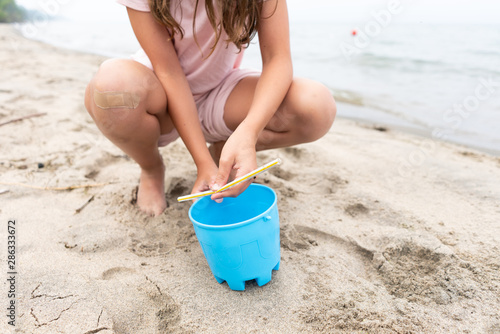 Girl Picking up Plastic Straw on Beach photo