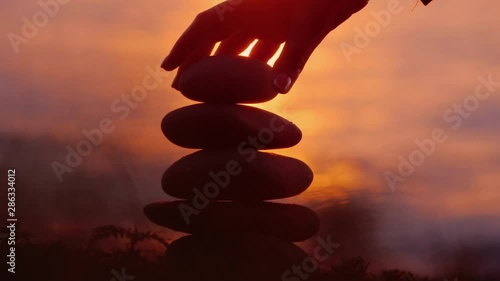 Focus on building a tower of stones against the background of the sea where the sun sets