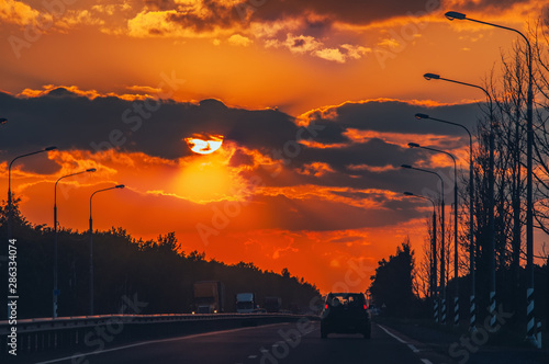 Highway with cars traveling on the sunset. Horizon line with the sun and storm clouds. Journeys. Selective focus