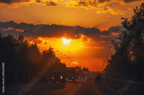 Highway with cars traveling on the sunset. Horizon line with the sun and storm clouds. Journeys. Selective focus © oksanamedvedeva